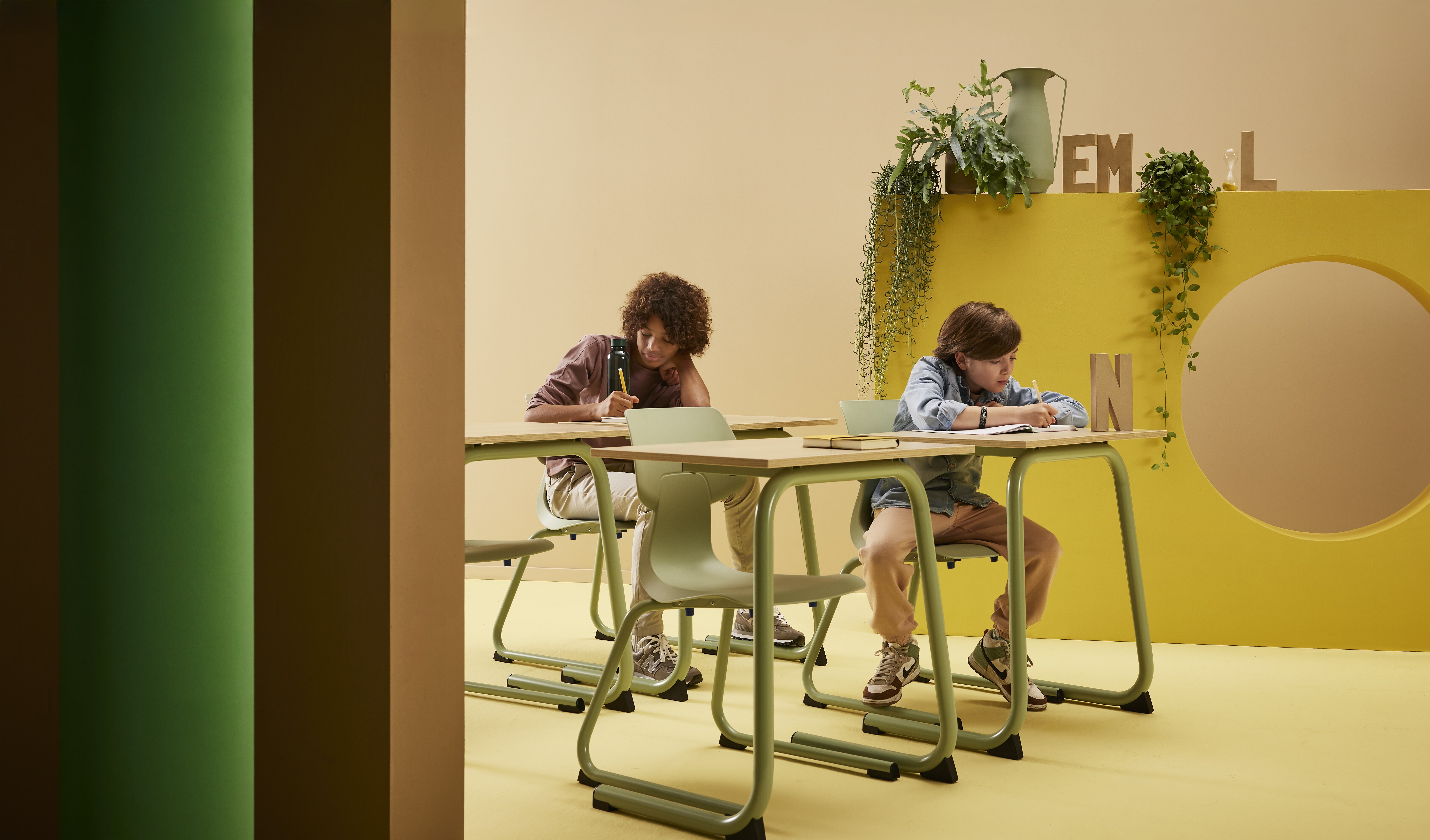 Gispen WIZZ c frame in green chairs with EDUU comfort tables with male models in a yellow green secondary education setting front left view kopiea